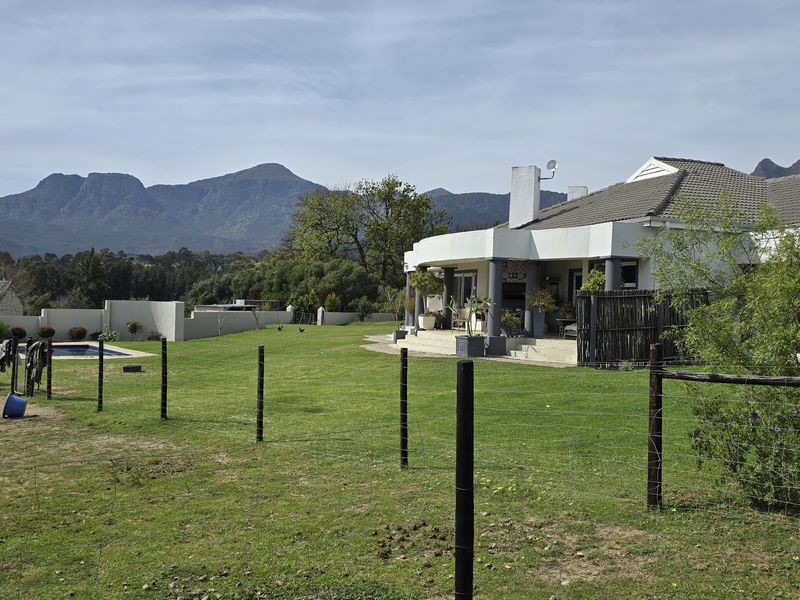 Rear view of the farm property featuring a spacious lawn, swimming pool, and a covered patio area set against a scenic mountain backdrop.