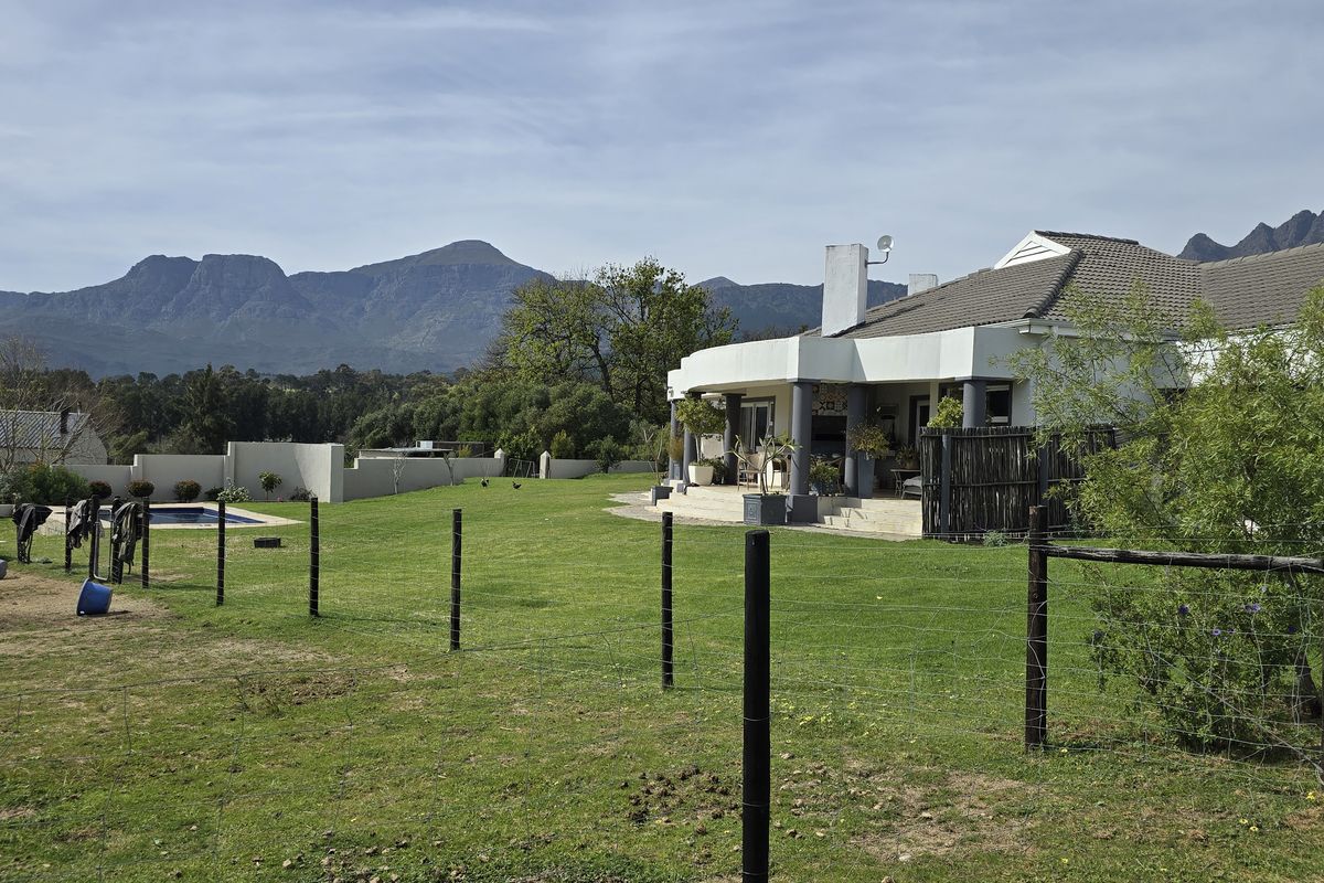 Rear view of the farm property featuring a spacious lawn, swimming pool, and a covered patio area set against a scenic mountain backdrop.