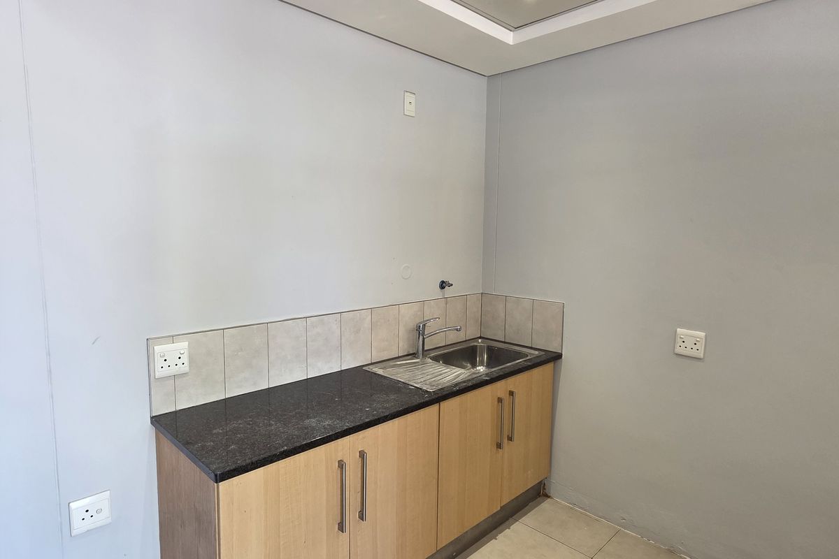 A compact kitchen area featuring light wood cabinetry, a dark granite countertop, a stainless steel sink, and tiled splashback.