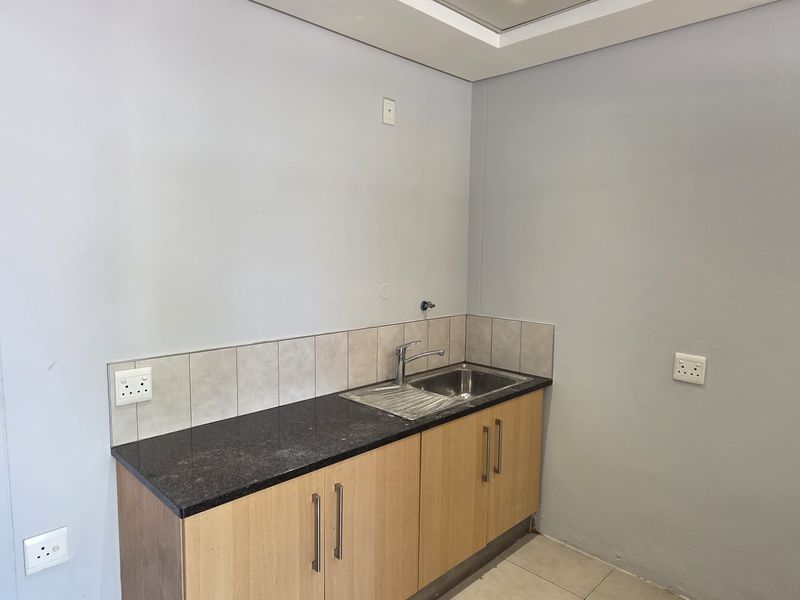 A compact kitchen area featuring light wood cabinetry, a dark granite countertop, a stainless steel sink, and tiled splashback.