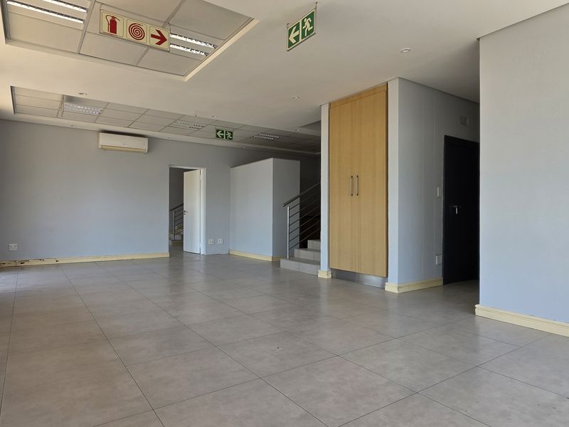 Spacious open-plan office area featuring tiled flooring, suspended ceilings, integrated air conditioning, and built-in storage, suitable for a professional workspace.