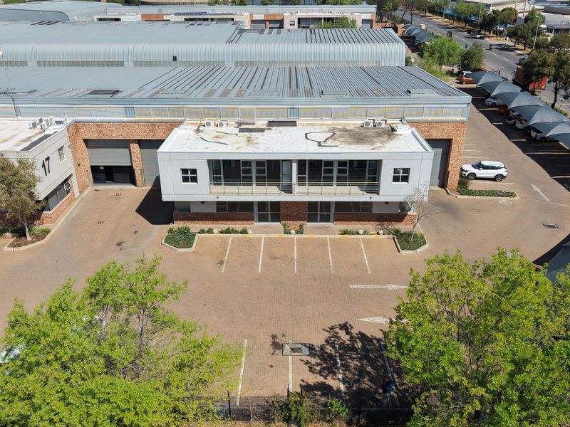 Aerial view of an industrial property featuring a large warehouse building, paved parking area, and office facade with balcony.