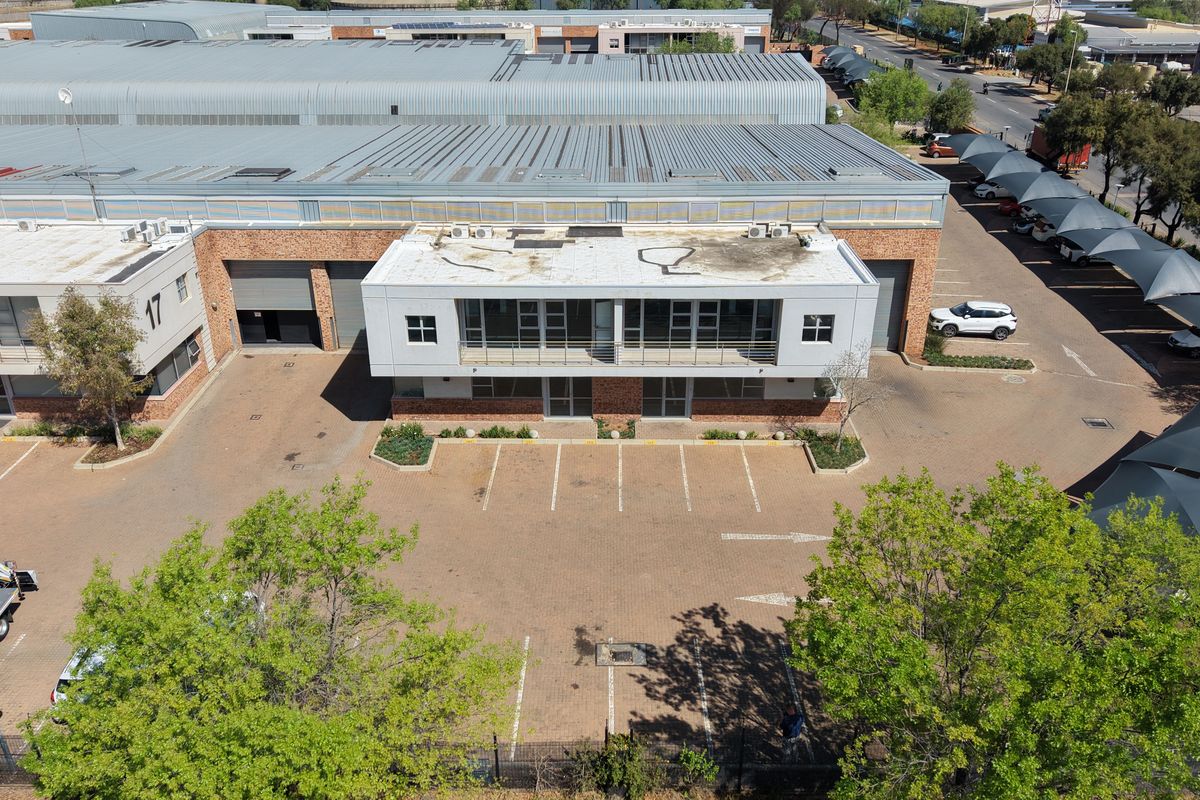 Aerial view of an industrial property featuring a large warehouse building, paved parking area, and office facade with balcony.