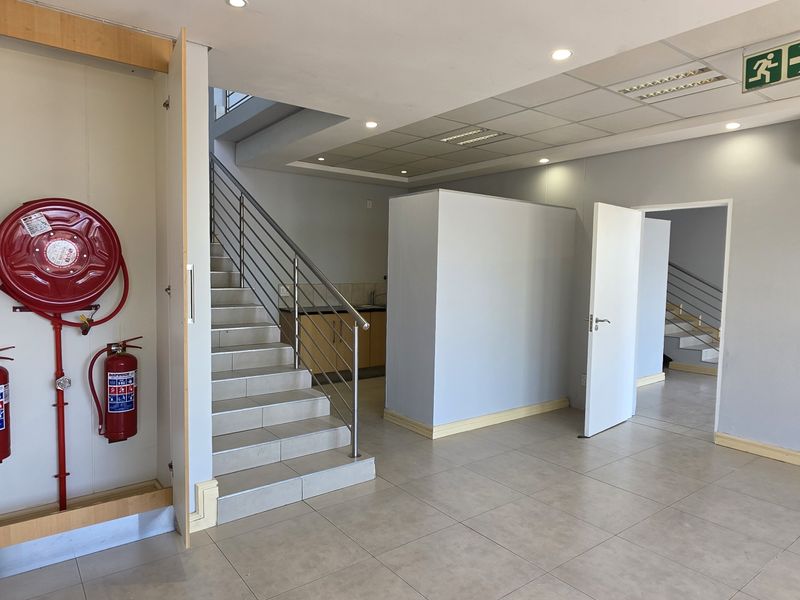 Spacious industrial entry area featuring tiled flooring, a staircase with stainless steel balustrade, integrated fire safety equipment, and a wall-mounted air conditioning unit.