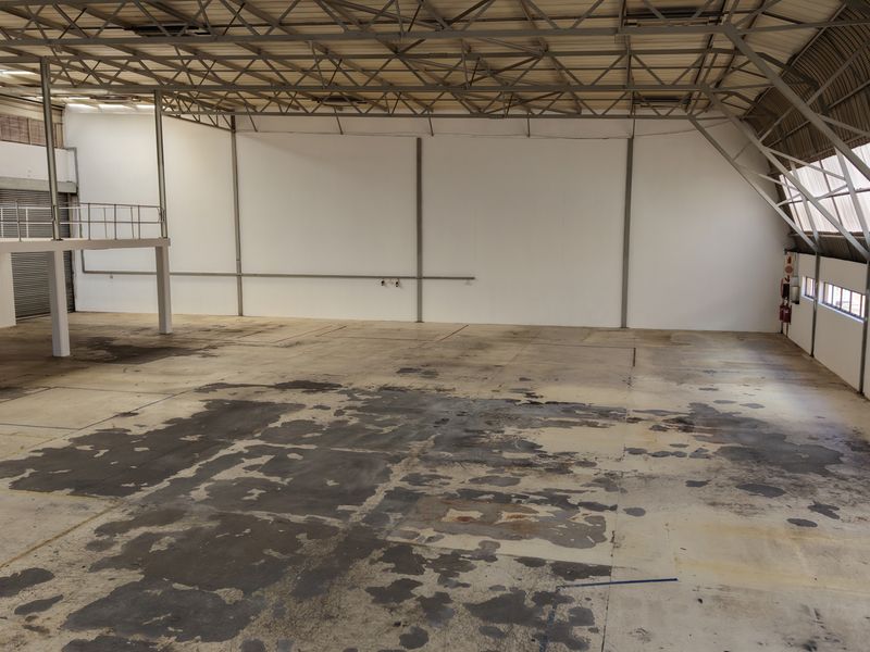 Spacious industrial warehouse featuring high ceilings with exposed steel trusses, a mezzanine level, and large open floor area suitable for various commercial operations.