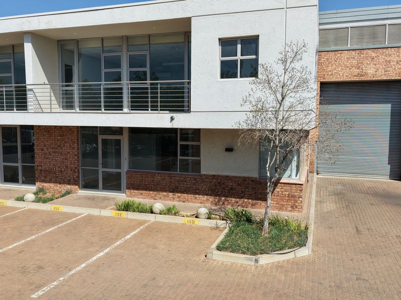 Front exterior view of an industrial property featuring a roller shutter door, brick and concrete facade, balcony, and dedicated paved parking bays.