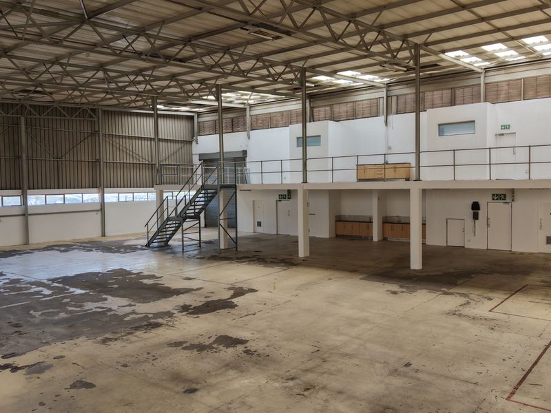 Spacious industrial warehouse featuring a high-clearance steel truss roof, mezzanine level with staircase, roller shutter access, and integrated storage cabinetry.