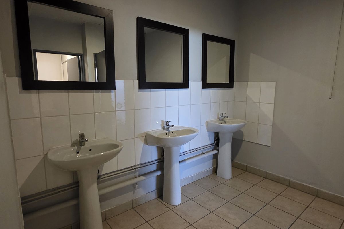 Functional industrial-style bathroom featuring three pedestal washbasins with tiled splashbacks and wall-mounted mirrors.