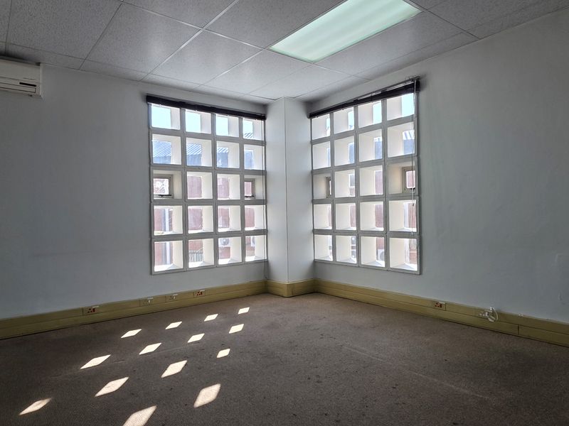 A vacant office space featuring a suspended ceiling, split-system air conditioning, and distinctive grid-pattern windows, providing a functional workspace with neutral finishes.
