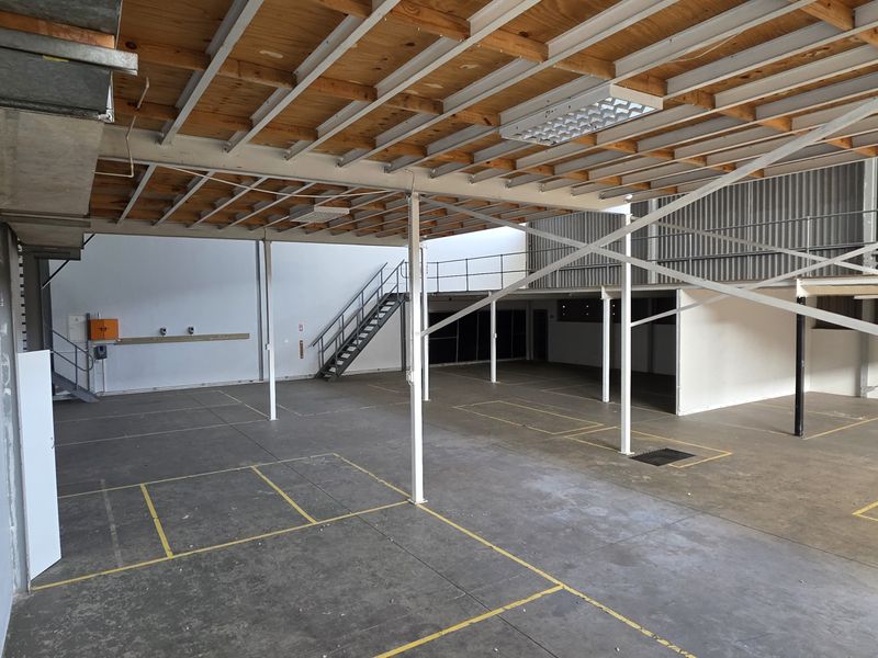 Spacious industrial utility area featuring exposed timber ceiling joists, steel support columns, a mezzanine level with metal staircase, and durable concrete flooring.