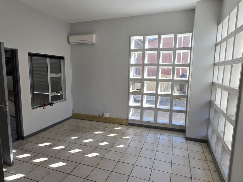 A bright, empty office space featuring tiled flooring, air conditioning, and distinctive glass block windows providing natural light.
