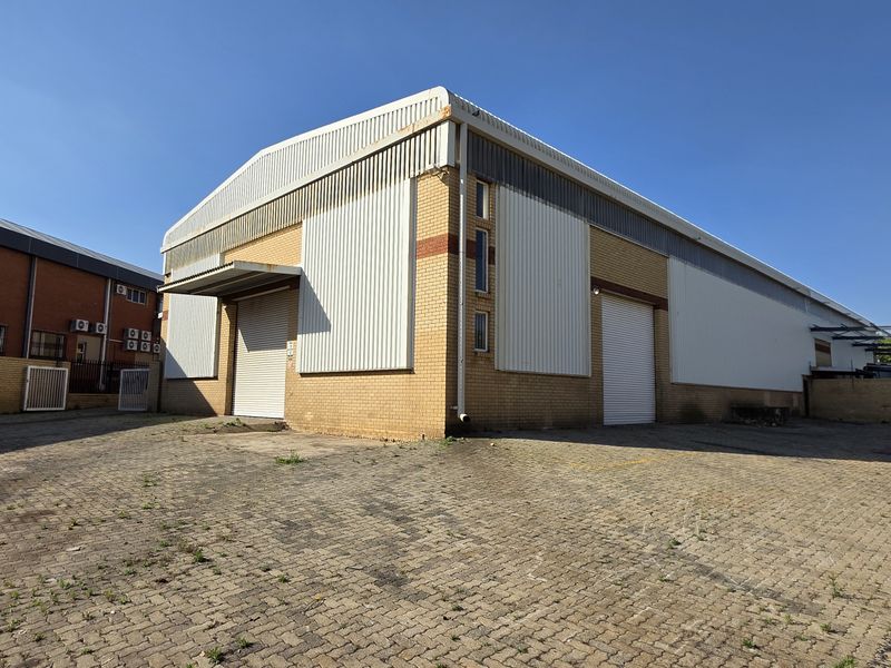 Industrial warehouse facility featuring dual roller shutter doors, brick and metal cladding construction, and a spacious paved yard area.