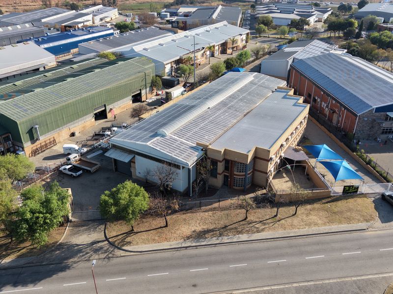 Aerial view of an industrial property featuring a large warehouse building, paved yard area, perimeter fencing, and shade structures in a commercial business park.