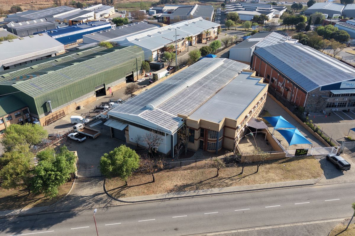 Aerial view of an industrial property featuring a large warehouse building, paved yard area, perimeter fencing, and shade structures in a commercial business park.