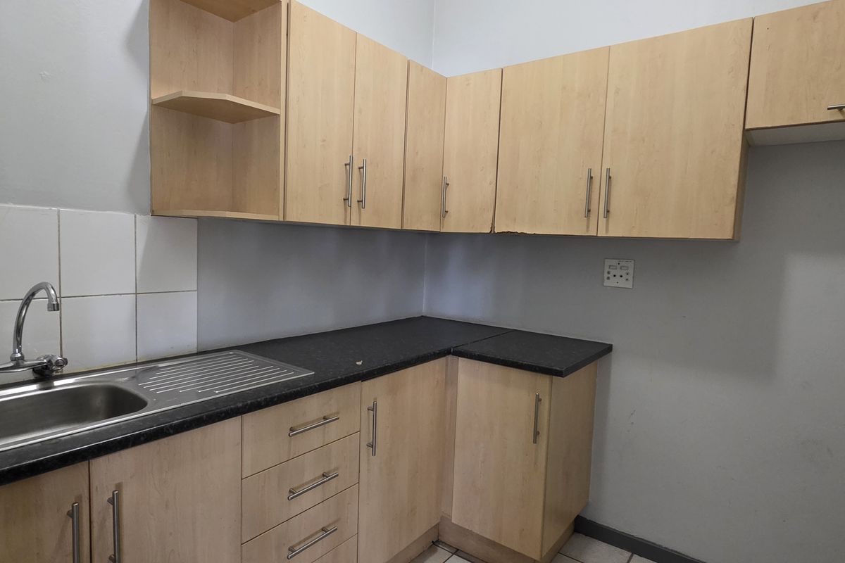 A functional kitchen area featuring light wood-tone cabinetry, dark laminate countertops, and a stainless steel sink with a tiled splashback.