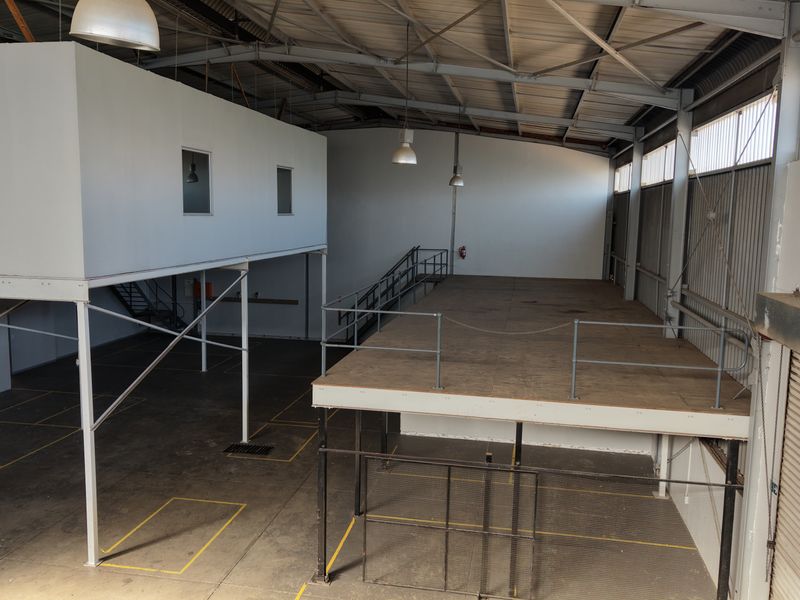Spacious industrial warehouse unit featuring a mezzanine level, high ceilings, concrete flooring, and a large roller shutter door for efficient access.