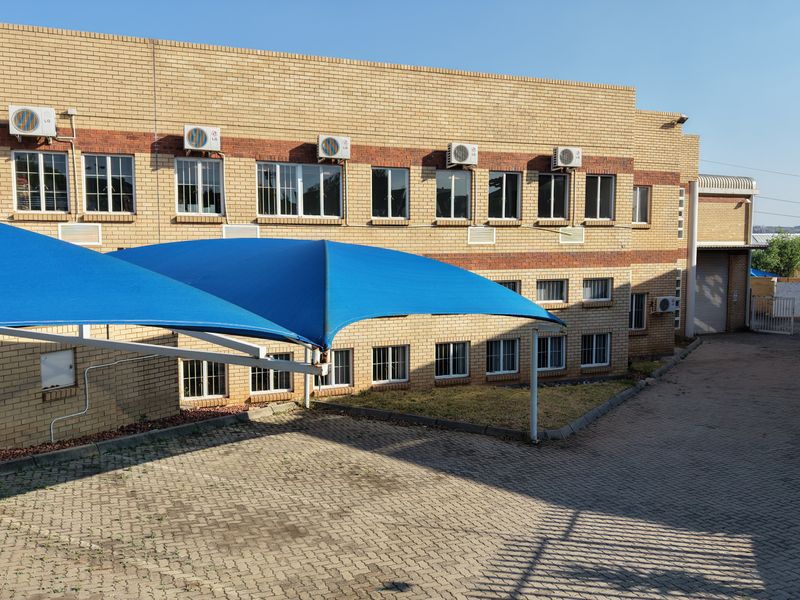 Rear exterior view of an industrial building featuring a brick facade, paved driveway, and blue shade sail parking structures.