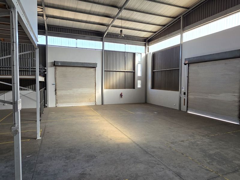 Spacious industrial warehouse unit featuring high ceilings, concrete flooring, dual roller shutter doors, and an integrated mezzanine level for additional storage or office space.