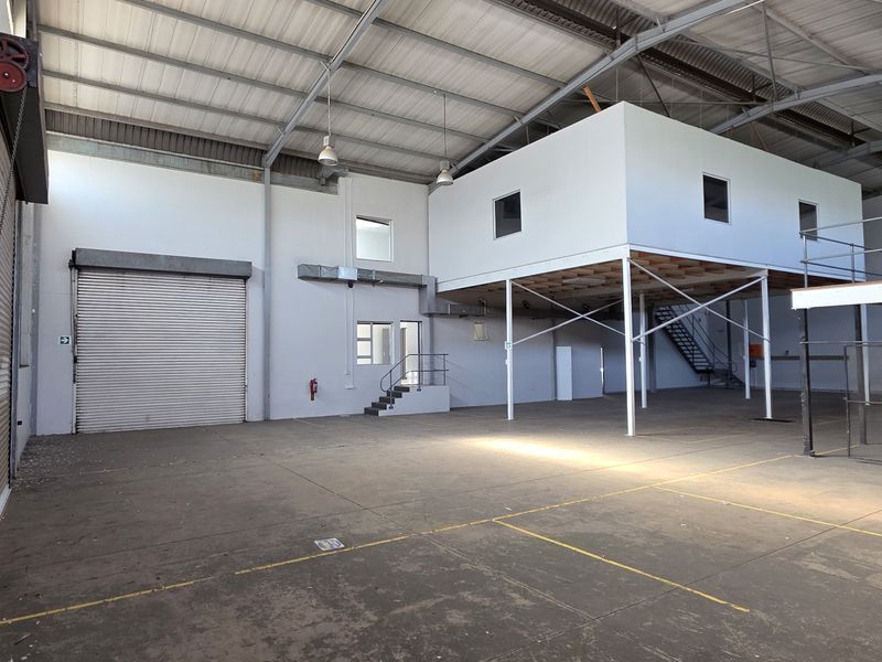 Spacious industrial warehouse featuring a high-clearance roof, concrete flooring, a large roller shutter door, and an integrated mezzanine level for additional storage or office space.