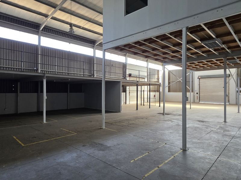 Spacious industrial warehouse unit featuring a mezzanine level, concrete flooring, steel structural columns, and a large roller shutter door for vehicle access.