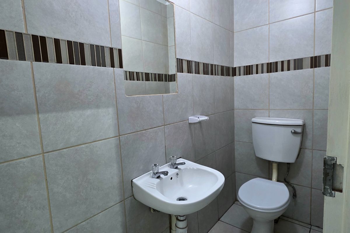 A functional bathroom featuring neutral ceramic wall and floor tiles, a pedestal washbasin, and a standard flush toilet.