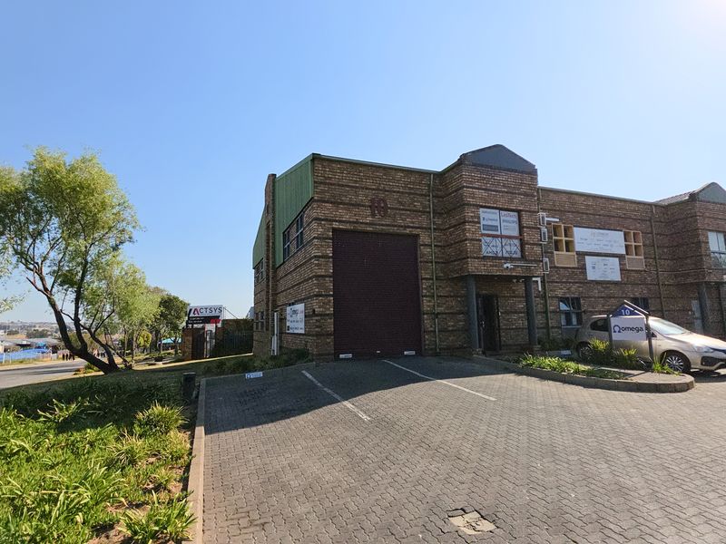 Front elevation of an industrial warehouse unit featuring a brick facade, large roller shutter door, and dedicated paved parking area.