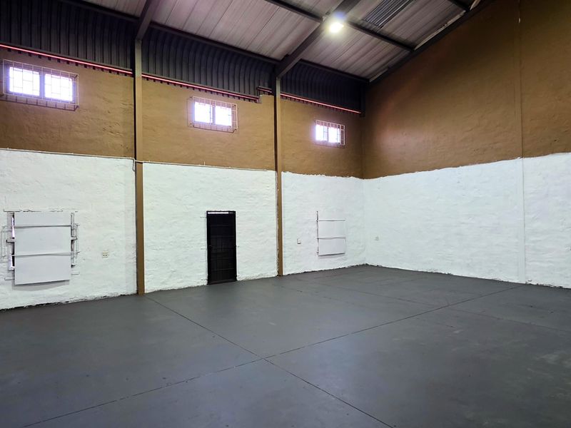 Spacious industrial utility area featuring high ceilings, exposed steel rafters, clerestory windows, and durable concrete flooring, suitable for storage or workshop use.