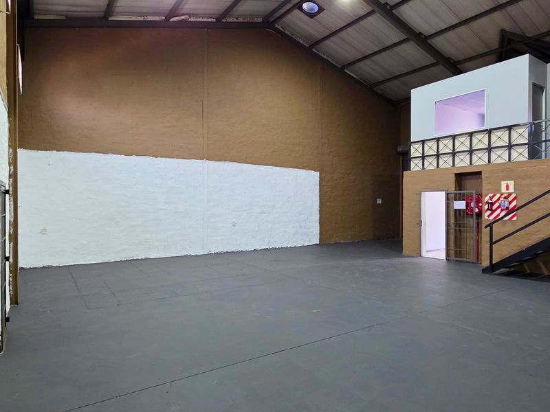 Spacious industrial warehouse unit featuring a mezzanine level, metal staircase, high exposed ceilings, and durable painted concrete flooring, suitable for various commercial operations.