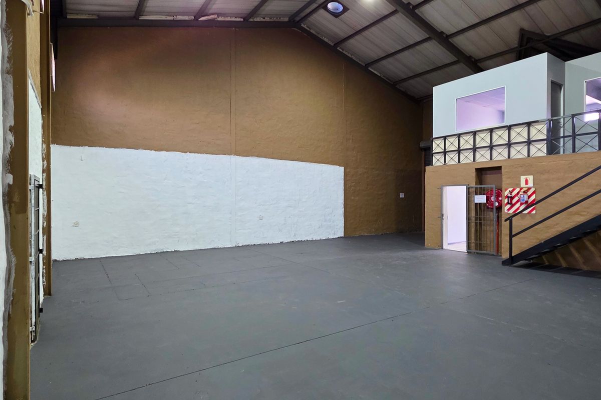 Spacious industrial warehouse unit featuring a mezzanine level, metal staircase, high exposed ceilings, and durable painted concrete flooring, suitable for various commercial operations.