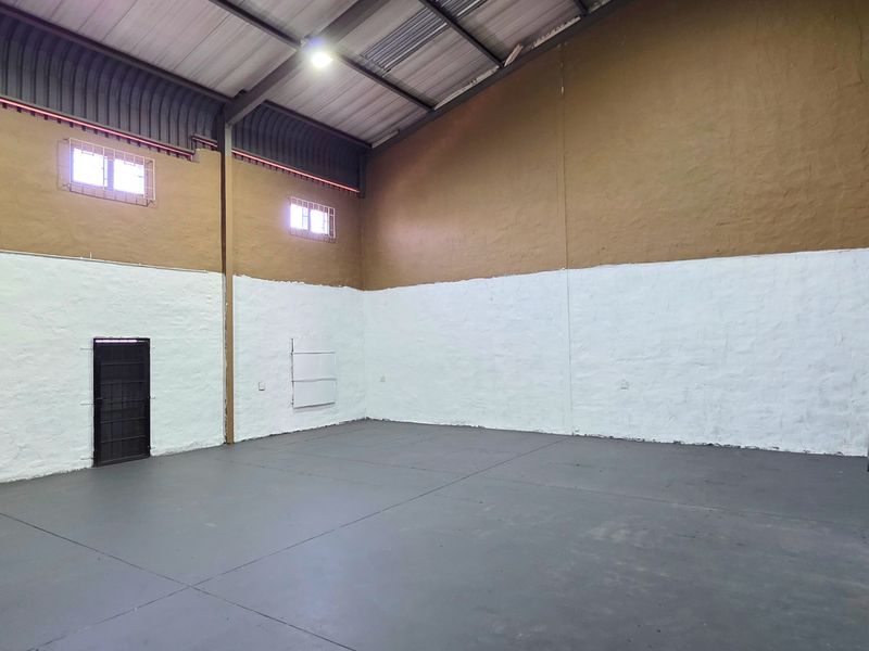 Spacious industrial utility area featuring high ceilings with exposed steel trusses, painted concrete flooring, and secure access points.