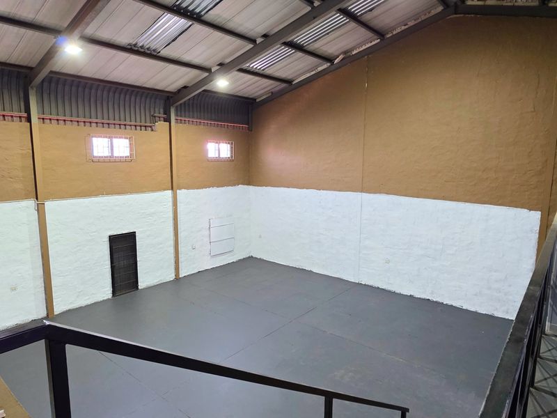 Spacious industrial utility area featuring high ceilings with exposed steel trusses, skylights, and durable painted masonry walls, viewed from a mezzanine level.