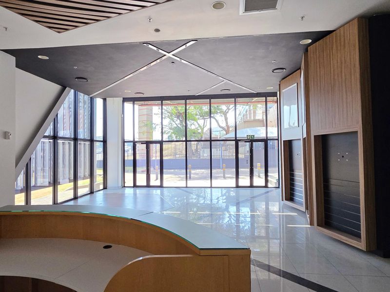 Modern industrial entrance lobby featuring a built-in reception desk, floor-to-ceiling glass windows, and high-quality tiled flooring with contemporary wood paneling accents.