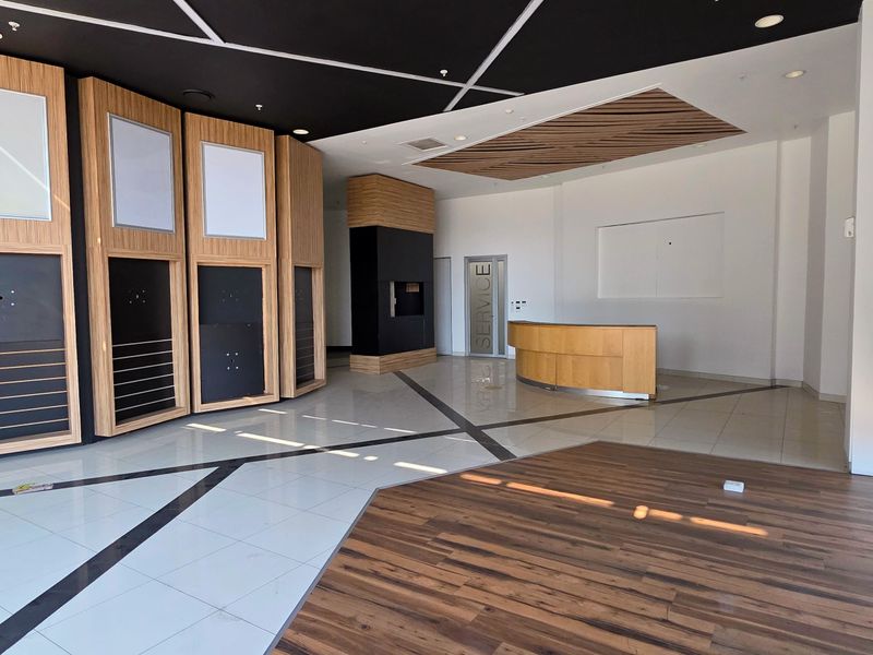 Spacious modern industrial reception area featuring a mix of tiled and wood flooring, built-in reception desk, and large windows providing ample natural light.