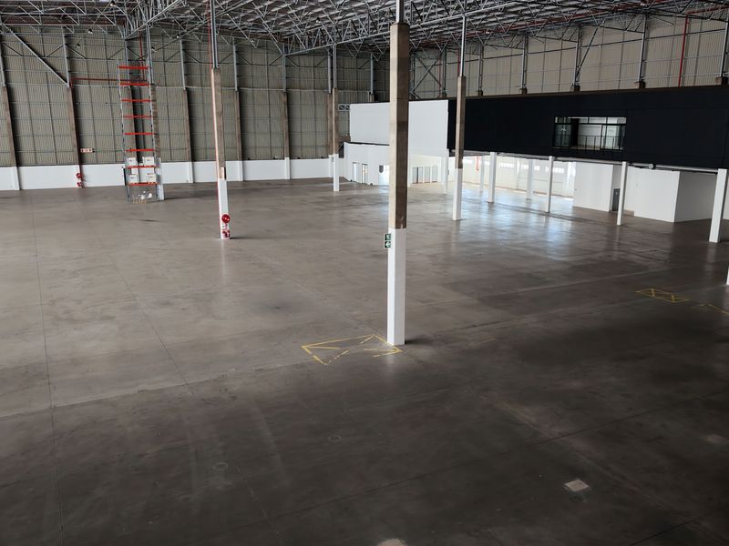 Spacious industrial warehouse featuring high ceilings with exposed steel trusses, polished concrete flooring, and a mezzanine level, suitable for various commercial operations.