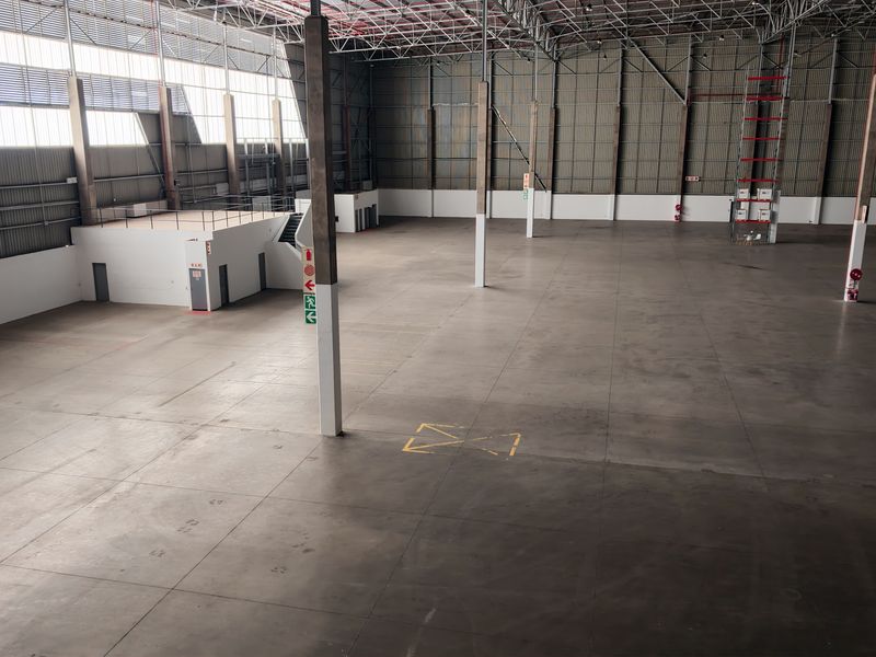 Spacious industrial warehouse featuring high ceilings, concrete flooring, steel support columns, a mezzanine level, and large clerestory windows for natural light.