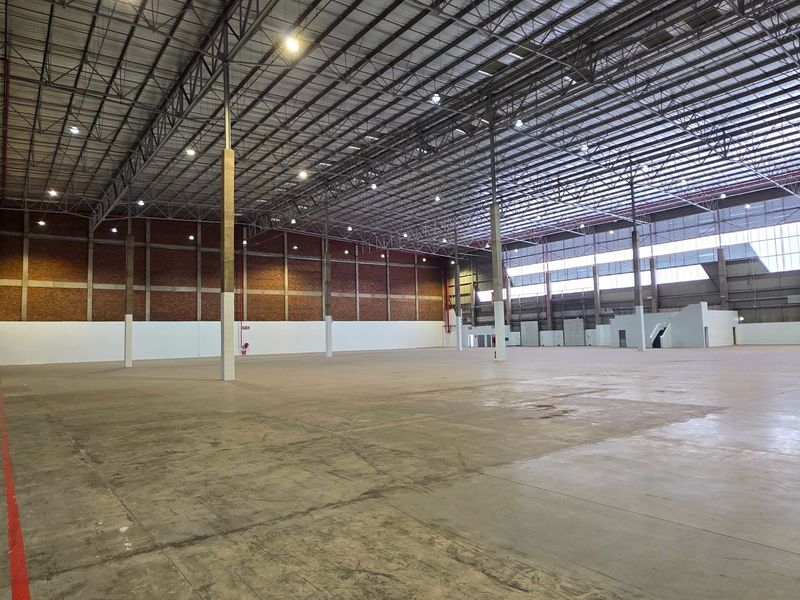 Expansive industrial warehouse space featuring high ceilings with exposed steel trusses, concrete flooring, and robust brick wall construction, suitable for logistics or manufacturing.