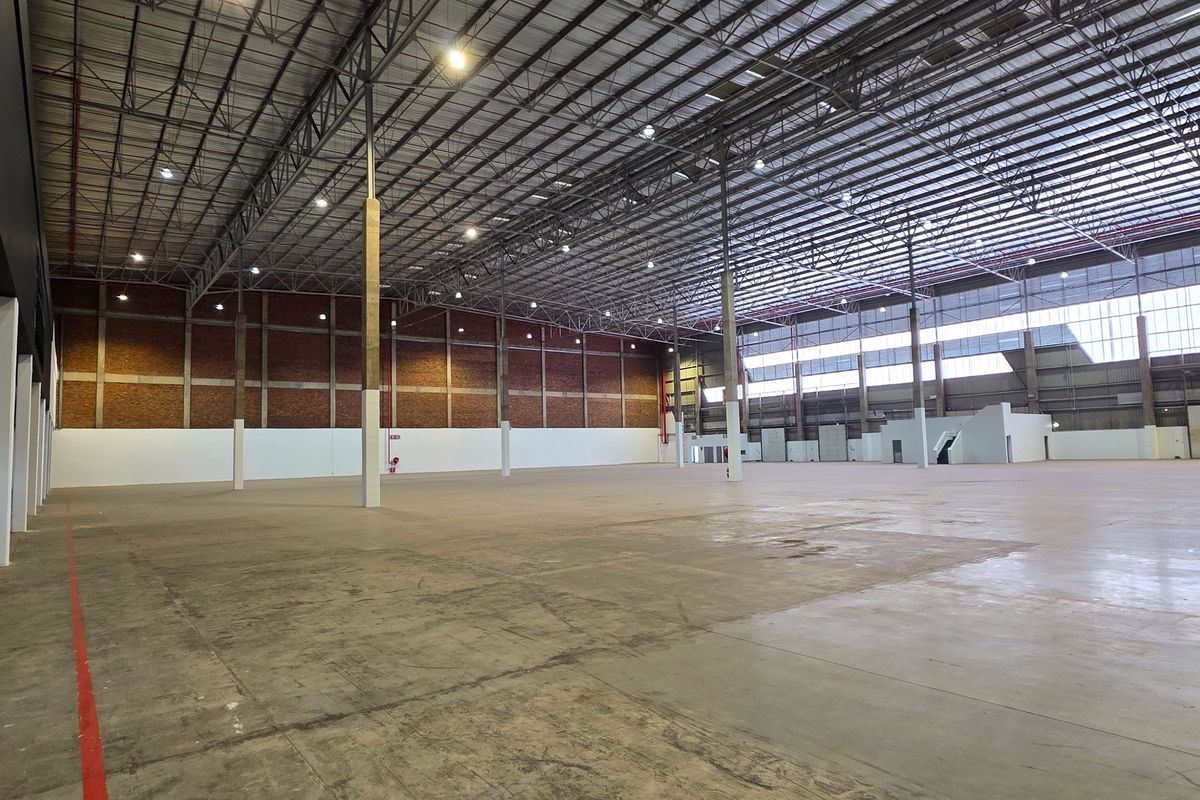 Expansive industrial warehouse space featuring high ceilings with exposed steel trusses, concrete flooring, and robust brick wall construction, suitable for logistics or manufacturing.