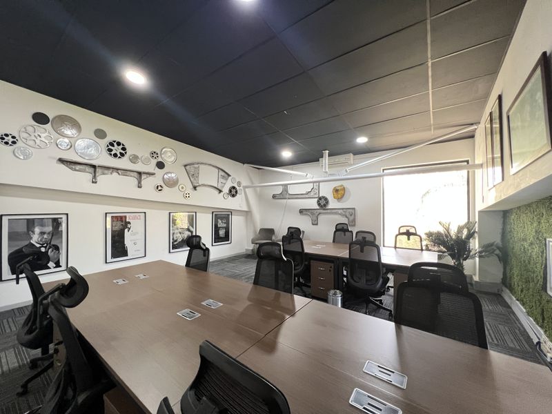 A modern office meeting room featuring a large central desk, suspended ceiling, recessed lighting, and integrated power connectivity.