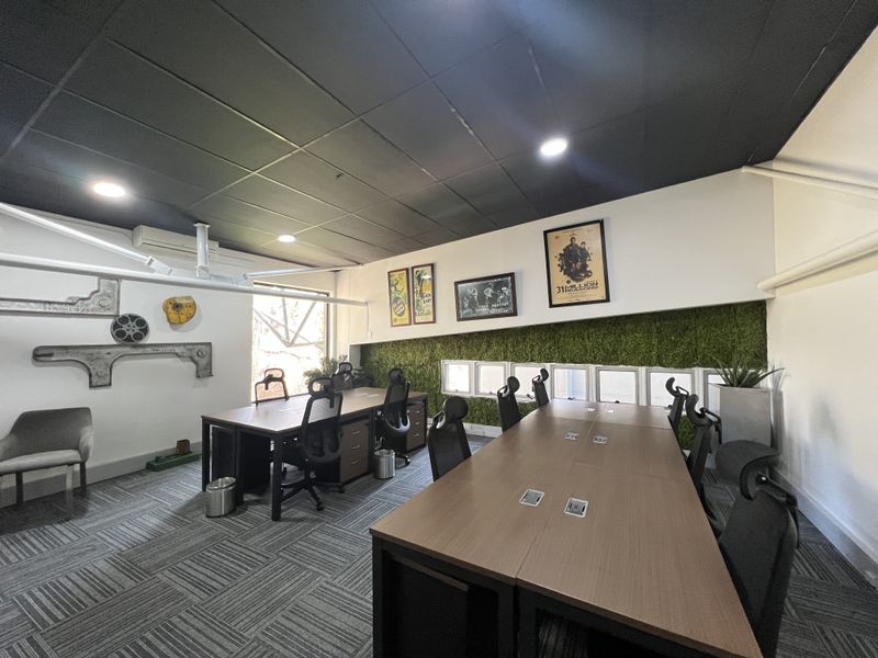 A modern office space featuring a suspended ceiling, recessed lighting, carpet tiles, and a decorative artificial grass wall feature.