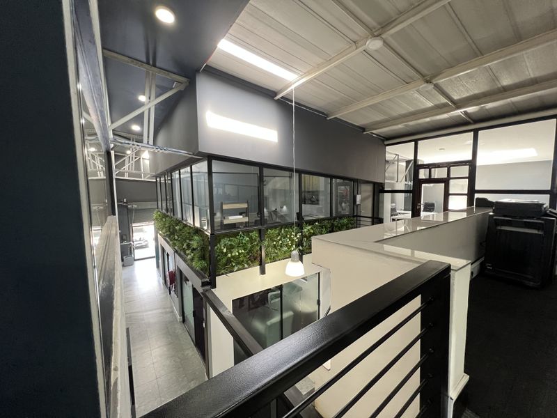 Modern office space featuring a mezzanine level with glass partitions, industrial-style metal roofing, and contemporary finishes throughout the workspace.