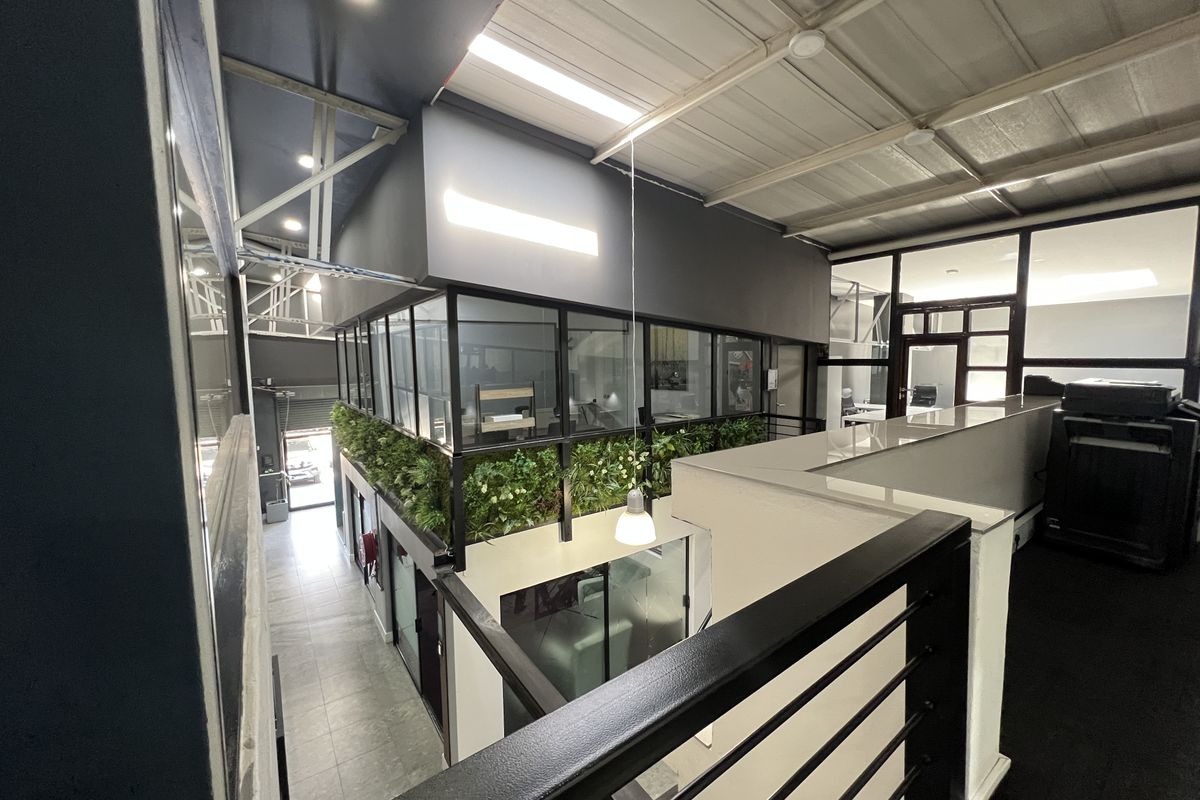 Modern office space featuring a mezzanine level with glass partitions, industrial-style metal roofing, and contemporary finishes throughout the workspace.