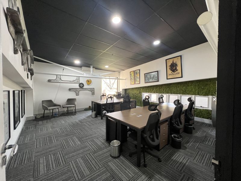 A modern office space featuring a suspended ceiling, carpet tile flooring, and a decorative moss feature wall, providing a professional work environment.