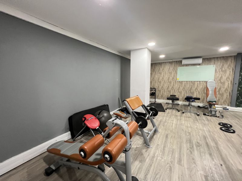 A well-maintained office gym space featuring laminate flooring, recessed lighting, and a wall-mounted air conditioning unit.