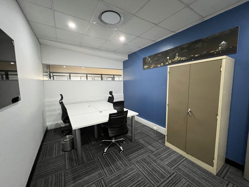 A functional office space featuring a suspended ceiling, recessed lighting, carpet tiles, and a built-in storage cabinet with a glass partition wall.