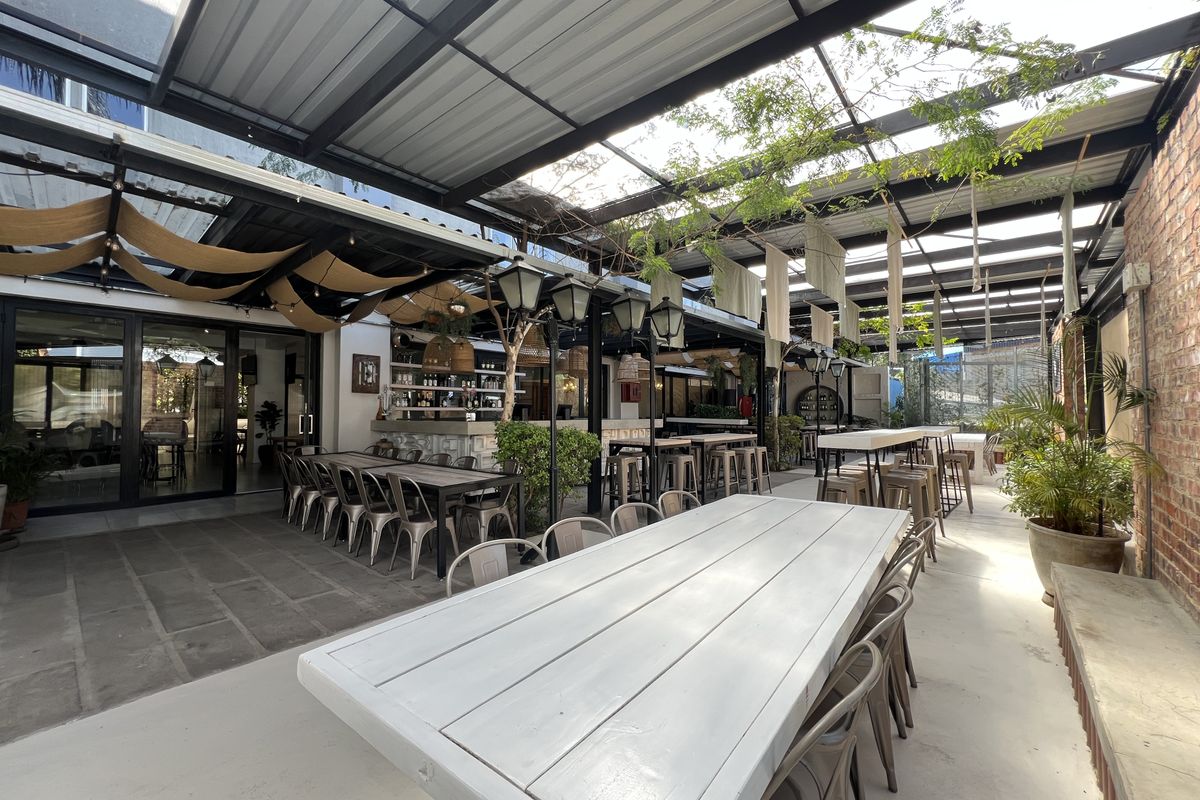 A spacious covered outdoor patio area featuring a metal roof structure, exposed brick wall, and a built-in bar counter, ideal for office social gatherings.