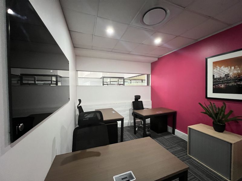 A functional office space featuring a suspended ceiling with recessed lighting, carpeted flooring, a glass whiteboard, and a vibrant accent wall.