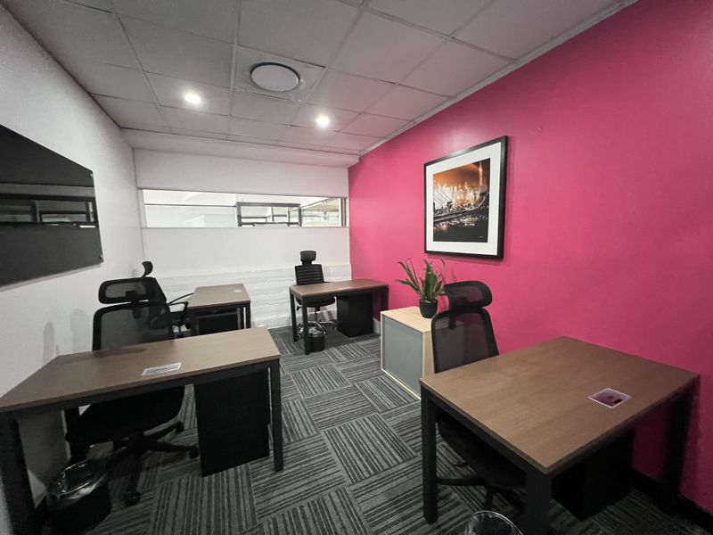 A functional office space featuring carpet tiles, a suspended ceiling with recessed lighting, and a distinctive accent wall.