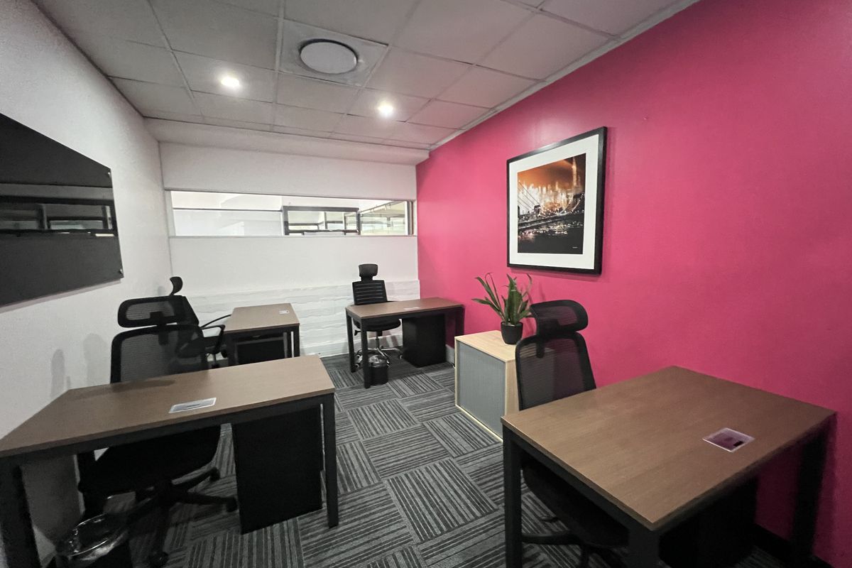 A functional office space featuring carpet tiles, a suspended ceiling with recessed lighting, and a distinctive accent wall.