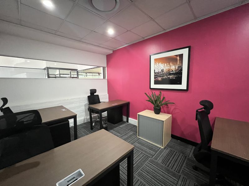 A functional office space featuring a bold accent wall, suspended ceiling with recessed lighting, and durable carpet tiles.