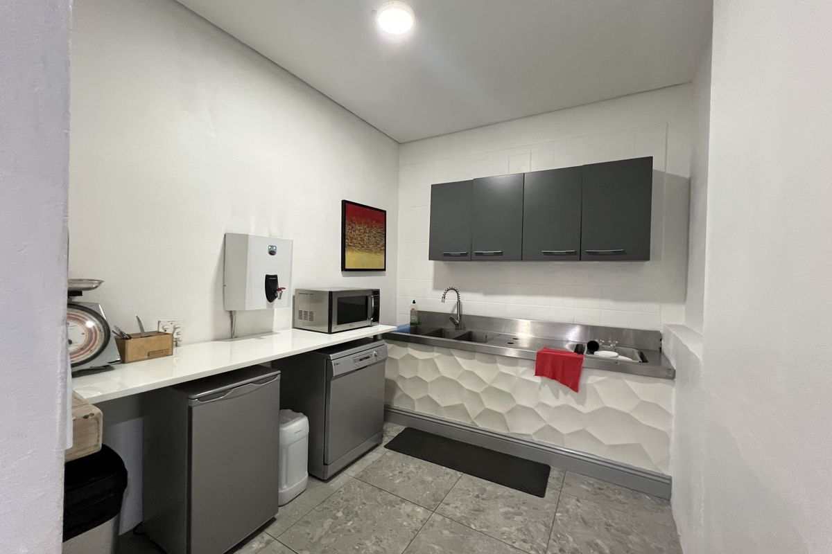 A functional office kitchenette featuring stainless steel sink, wall-mounted cabinetry, textured wall detailing, and tiled flooring.